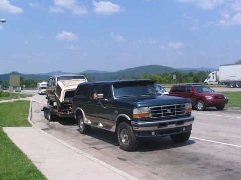 1986 Ford C-350 (Centurion Conversions) - A dark green Ford Bronco tows a trailer carrying a white van body on a sunny day.