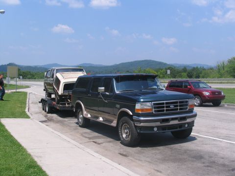 1986 Ford C-350 (Centurion Conversions) - Green Ford Bronco SUV tows a trailer with a pickup truck bed on a sunny day.