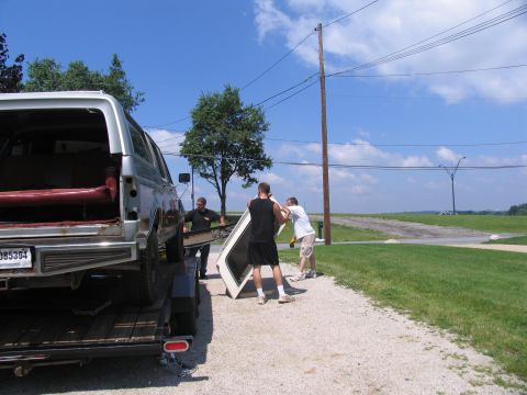 1986 Ford C-350 (Centurion Conversions) - Men remove the roof from a silver Ford Bronco loaded onto a trailer.