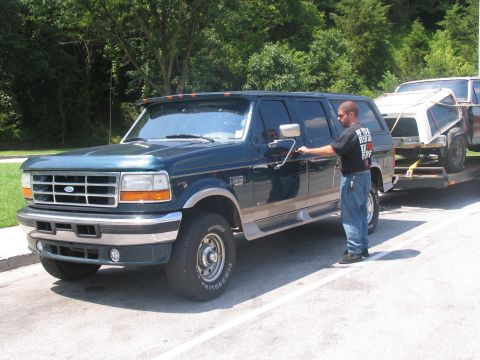 1986 Ford C-350 (Centurion Conversions) - A dark green SUV, likely a 1992 Ford Centurion conversion, is seen being towed on a trailer.