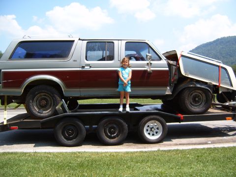 1993 Ford Bronco - A young girl stands next to a two-tone SUV being transported on a trailer.