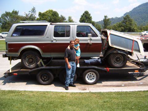 1993 Ford Bronco - A man and child stand beside a 1993 Ford Bronco being transported on a trailer with its removable top detached.