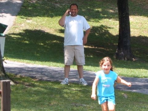 1993 Ford Bronco - A man talks on his phone while a young girl runs past him in a park setting.