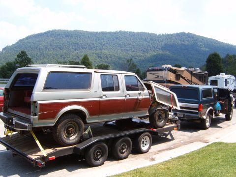 1993 Ford Bronco - A damaged SUV is being transported on a trailer, with other vehicles and RVs in the background.