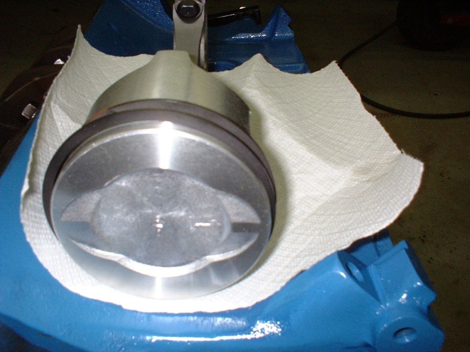 Engine piston with connecting rod, resting on paper towel over blue engine block