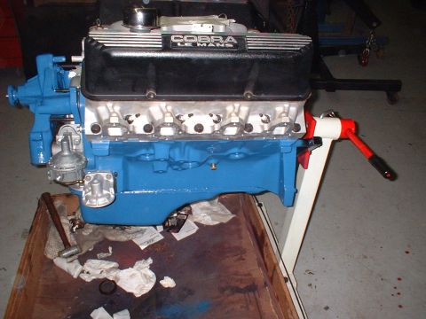 1965 Shelby Cobra - A blue engine with black valve covers labeled "Cobra Le Mans" is mounted on a stand.
