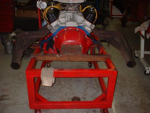 1965 Shelby Cobra - V8 engine with dual exhaust manifolds on a red rolling stand in a workshop.