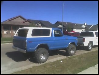 1995 Ford Bronco - This blue Bronco with a white top and oversized tires is seen from a 3/4 front angle, parked on a residential street.