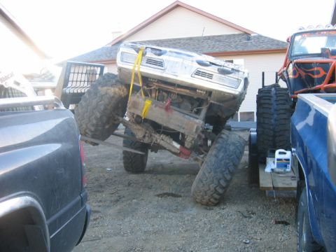 1995 Ford Bronco - A heavily modified truck with large tires is being transported, tilted on a trailer.