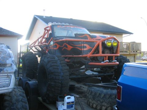 1995 Ford Bronco - Custom off-road truck with extensive modifications, including a roll cage and flame graphics, is parked on a trailer.