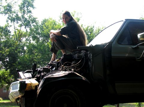 1986 Ford C-350 (Centurion Conversions) - Person sits on the engine of a truck with the hood open, outdoors.