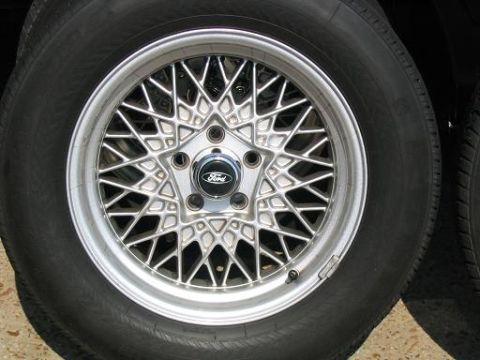 1999 Ford Crown Victoria - A detailed view of a silver wire-style wheel with a Ford logo on the center cap.