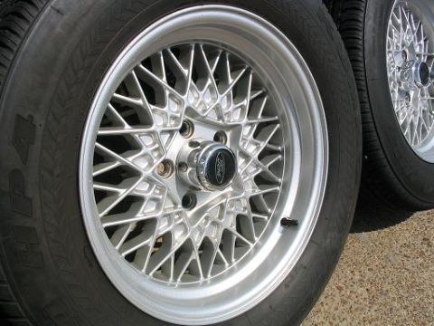 1999 Ford Crown Victoria - Close-up view of silver mesh wheels, one a Ford logo center cap, alongside tires.