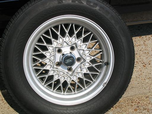 Close-up of a silver wire-spoke wheel with a black tire and a Ford center cap