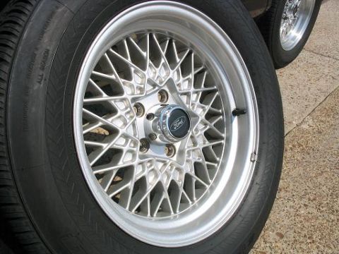 1999 Ford Crown Victoria - A close-up view of a silver mesh wheel with a Ford emblem, alongside another wheel in the background.