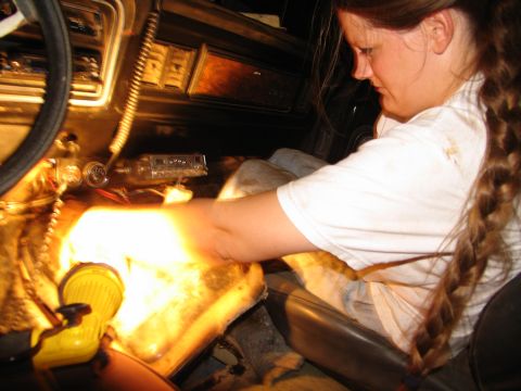 1978 Ford Bronco - A person works on the transmission tunnel of a vehicle, illuminated by a yellow flashlight.
