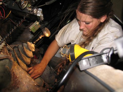 1978 Ford Bronco - A woman works on the transfer case inside a vehicle, illuminated by a work light.