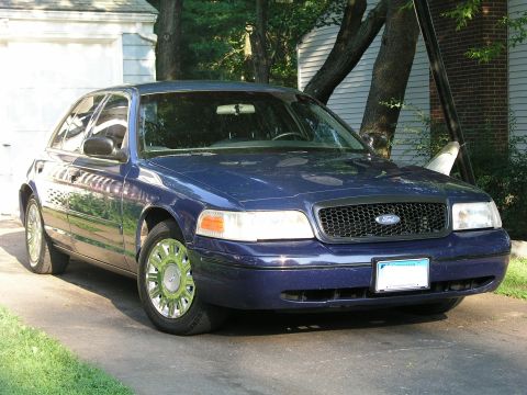 1999 Ford Crown Victoria - A blue 1999 Ford Crown Victoria is parked in front of a garage.