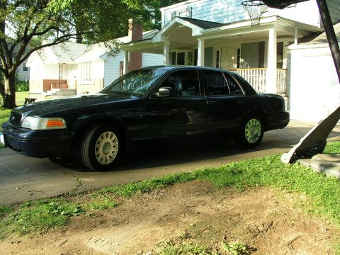 1999 Ford Crown Victoria - A black Ford Crown Victoria is parked on a driveway in front of a house on a sunny day.