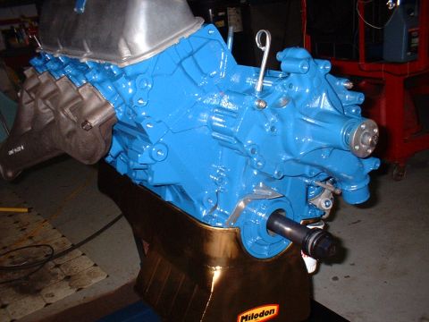 1970 Ford Torino - A bright blue engine, likely a performance V8, is mounted on a stand with a gold oil pan. Text on the stand reads 'SUPERMOTORS'.