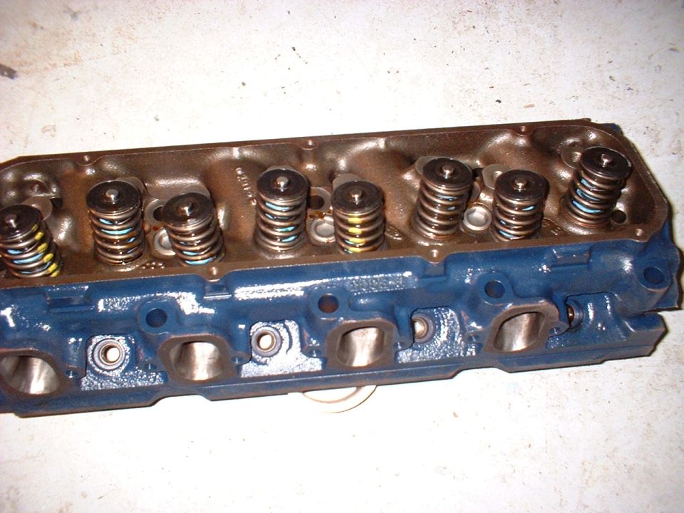 Blue-painted cast-iron V8 cylinder head with assembled valve springs on a concrete floor