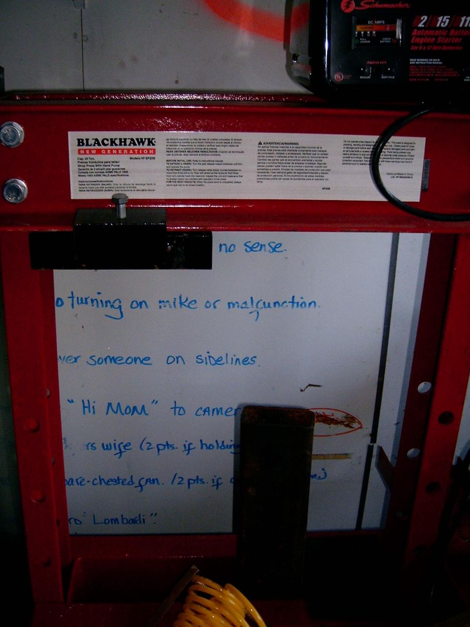 Red hydraulic press with a whiteboard displaying handwritten notes