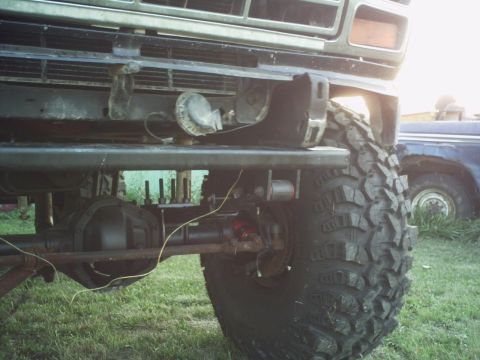 1986 Ford Bronco - Close-up of a truck's front suspension and tire, with another vehicle in the background.