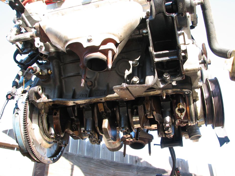 Engine block with crankshaft and connecting rods visible, mounted on a wooden surface
