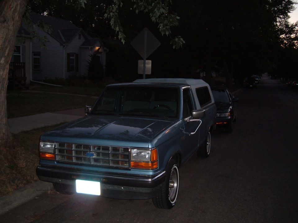 Blue Ford Bronco II parked on street, another car behind it