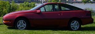 1991 Ford Probe - This 1991 Ford Probe is shown in a side profile, parked on grass with a body of water and buildings in the background.