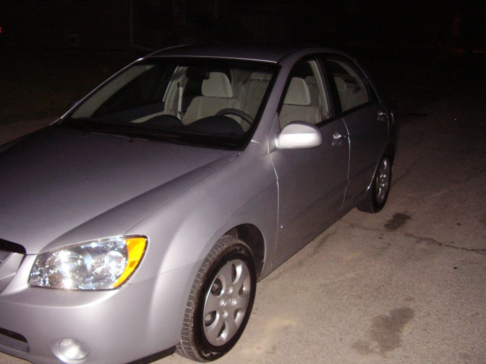 Silver sedan parked on concrete, front 3/4 view. Headlights and side mirror visible