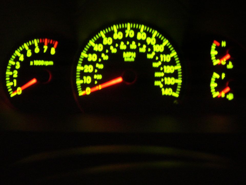 Car dashboard with glowing green gauges, including a speedometer and tachometer