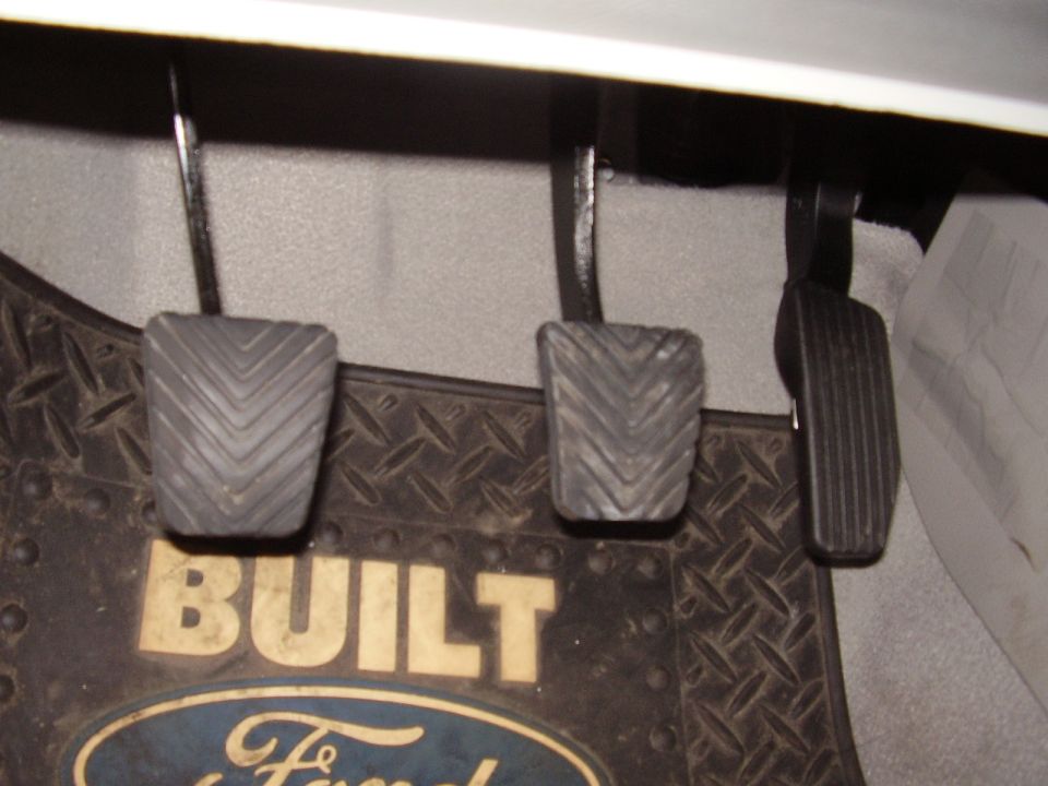 Close-up of three pedals and a Ford floor mat inside a vehicle