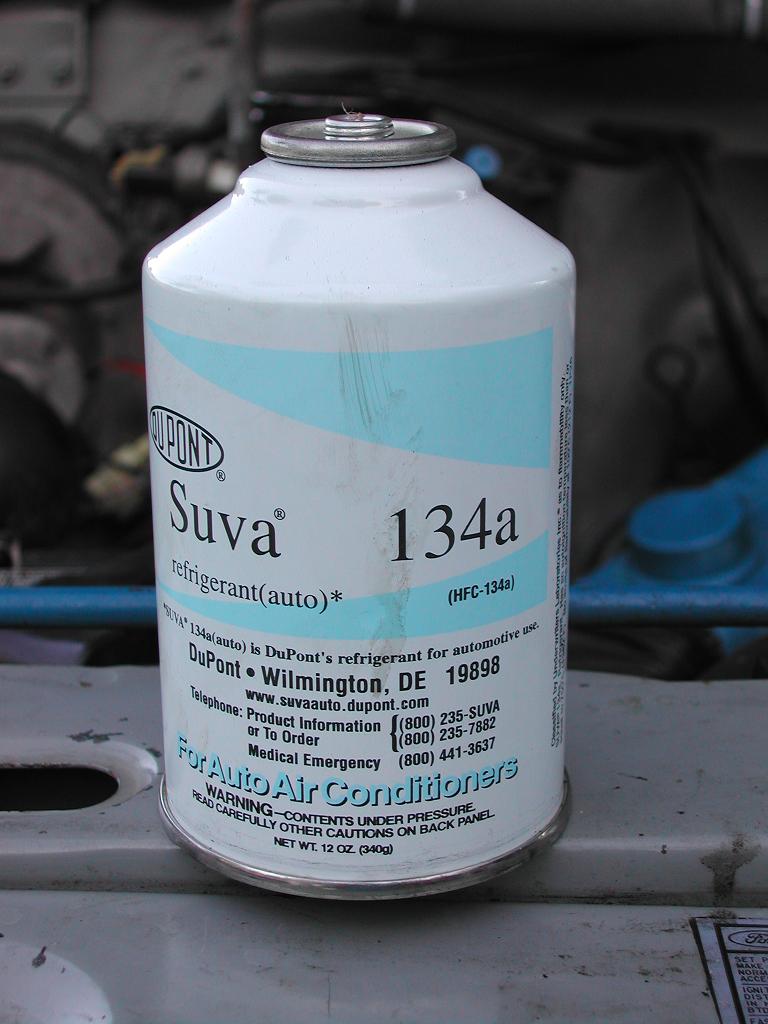DuPont Suva 134a automotive A/C refrigerant can held over an engine bay