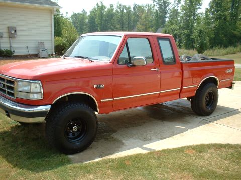 1995 Ford F-150 - Red Ford F-150 extended-cab short-bed pickup parked on a concrete driveway, shown from the front-left with F-150 fender badging and a 4x4 d…