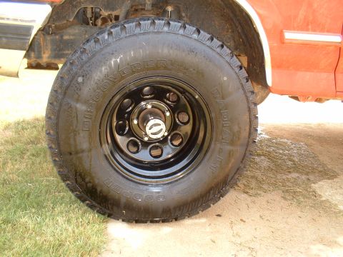 1995 Ford F-150 - Straight-on close-up of a freshly dressed Cooper Discoverer radial all-terrain tire on a black eight-slot steel wheel with a small chrome c…