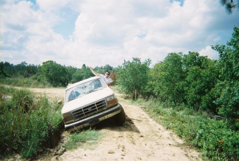 1995 Ford Bronco - A 1995 Ford Bronco is stuck in a ditch on a dirt road, with a person waving from the driver's side window.