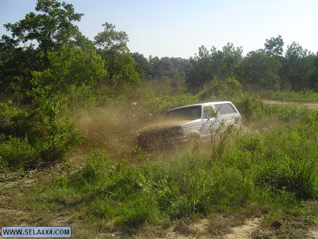 White SUV kicking up mud while driving off-road through tall grass and bushes