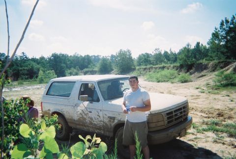 1995 Ford Bronco - A man stands beside a dirty white Ford Bronco in an outdoor, off-road setting.