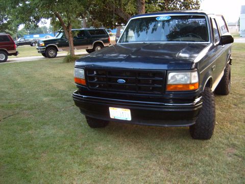 1993 Ford Bronco - A dark blue 1993 Ford Bronco is parked on a grassy lawn with other vehicles in the background.