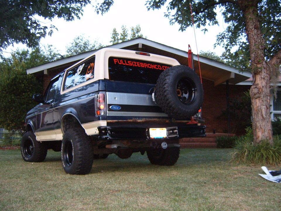 Rear view of lifted Ford Bronco with spare tire on back. "FULLSIZEBRONCO.COM" sticker on rear window