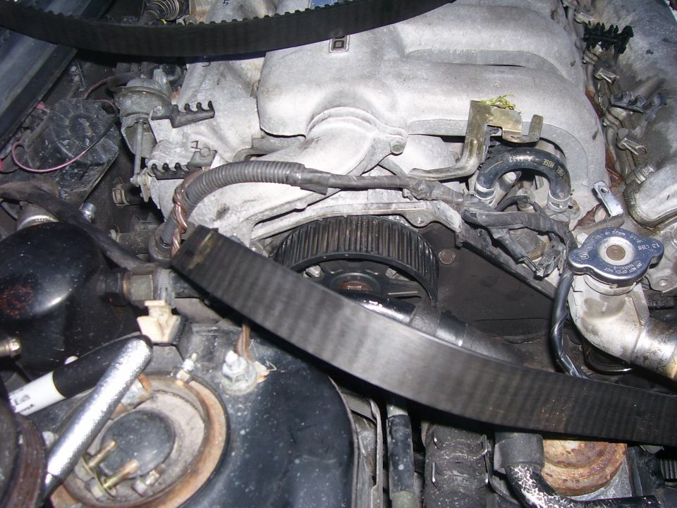Engine timing belt and pulley system, close-up view. Visible hoses and engine components