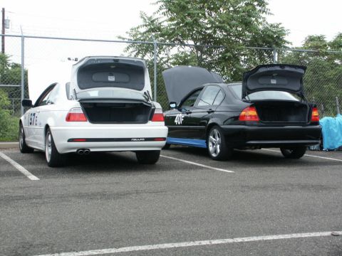 2001 Mercury Grand Marquis - Two BMW sedans, one white and one black, are parked with their trunks open. The white car has a '1976' decal, and the black car has a '40F'…