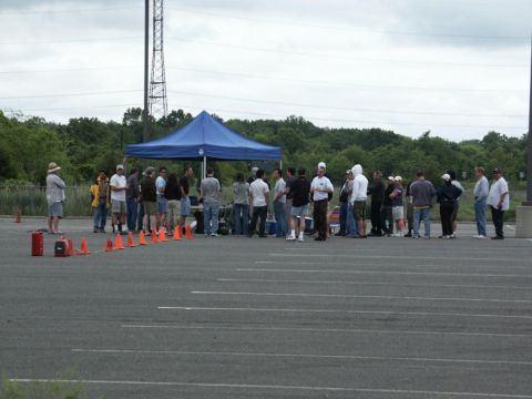2001 Mercury Grand Marquis - A group of people are gathered in an open paved area, with a blue tent set up and orange cones marking a path.