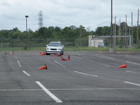 2001 Mercury Grand Marquis - Silver sedan driving through an obstacle course in a parking lot with industrial buildings in the background.
