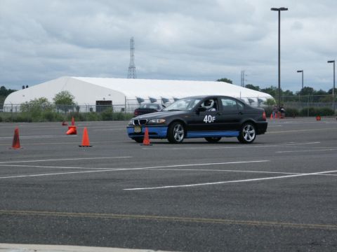 2001 Mercury Grand Marquis - A black sedan with blue trim and racing numbers navigates a course marked by orange cones, with another vehicle visible in the background.