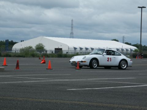 2001 Mercury Grand Marquis - A white Porsche 911 with racing number 21 navigates a course marked by orange cones under a cloudy sky.
