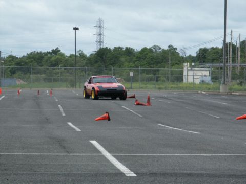 2001 Mercury Grand Marquis - A red sports car with gold wheels drives through a cone course in an asphalt lot under a cloudy sky.