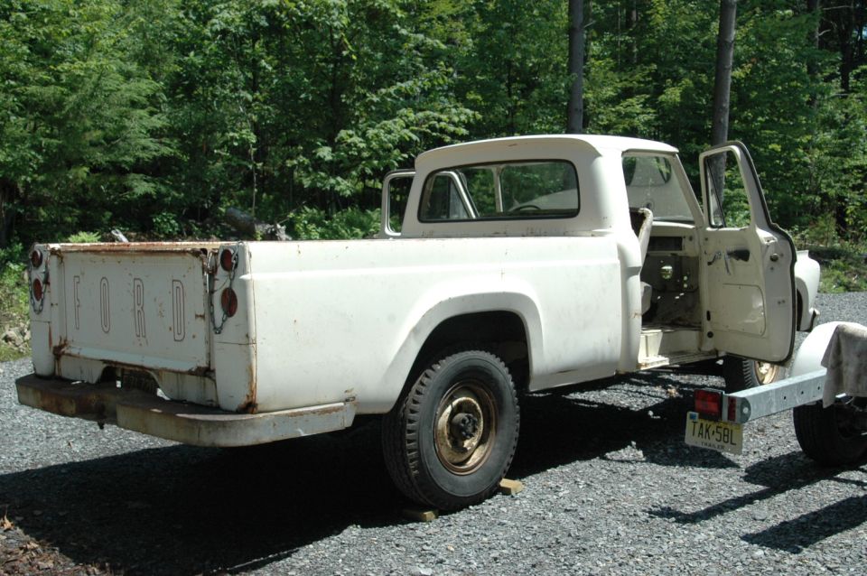 White Ford pickup truck with "FORD" tailgate, doors open, on gravel
