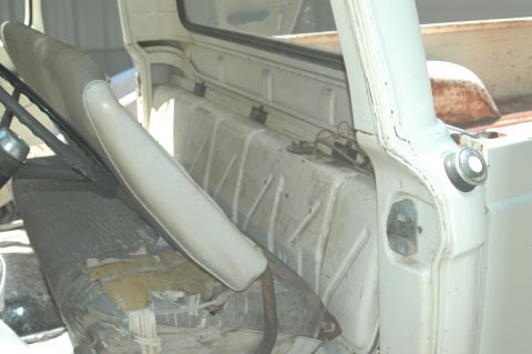 1963 Ford F-250 - The interior of a white pickup truck reveals a worn bench seat and ribbed metal paneling.